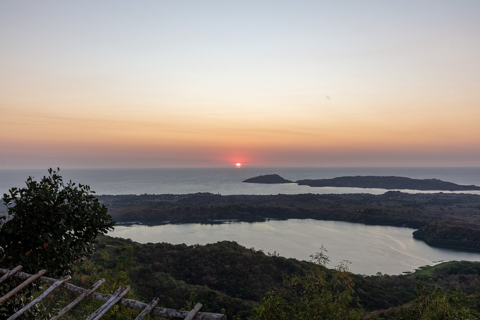 A red sun dropping to the horizon above a crater lake